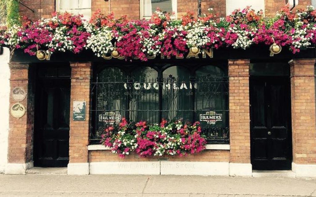 Photo of the exterior of Coughlan's bar. Flower baskets are hanging over the name and on the window.
